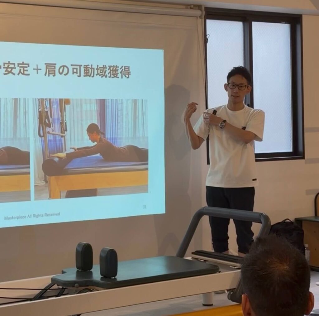 ピラティススタジオBB 恵比寿にて、肩関節対策のピラティスセミナーを開催している際に、パフォーマンスアップピラティスのマスタートレーナーの大岩俊貴がプロジェクターの前で肩の可動域の解説をしている写真